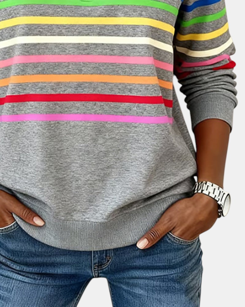 Sweater Margaret Dublin cinzento com riscas horizontais coloridas e ajuste relaxado, usado com calças de ganga.