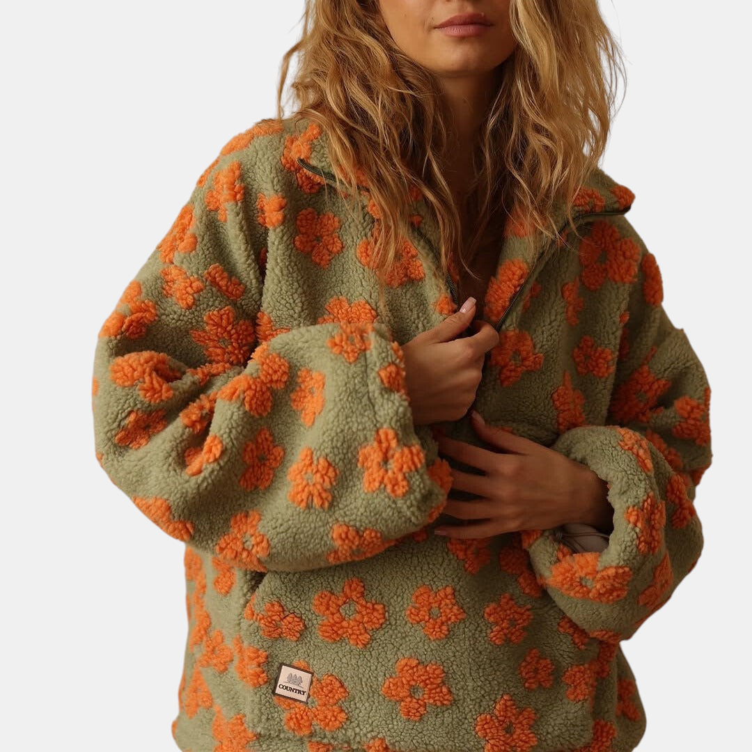 Casaco Margaret Dublin Daisy de fleece sherpa verde com padrão floral laranja, corte oversized e fecho frontal.