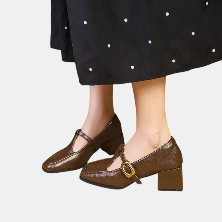 Sapatos Margaret Dublin Ida castanhos com salto médio, tira frontal e fivela dourada, usados com saia às bolinhas.