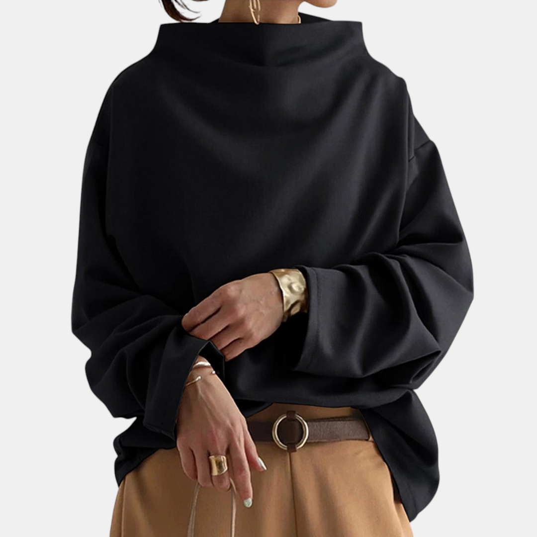 Woman wearing the Margaret Dublin Agnès black jumper with high neck and relaxed fit, paired with brown trousers.