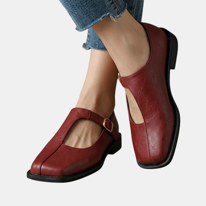 Sapatos Margaret Dublin Rosalie estilo bailarina em pele vermelha com tira e fivela, usados com calças de ganga.